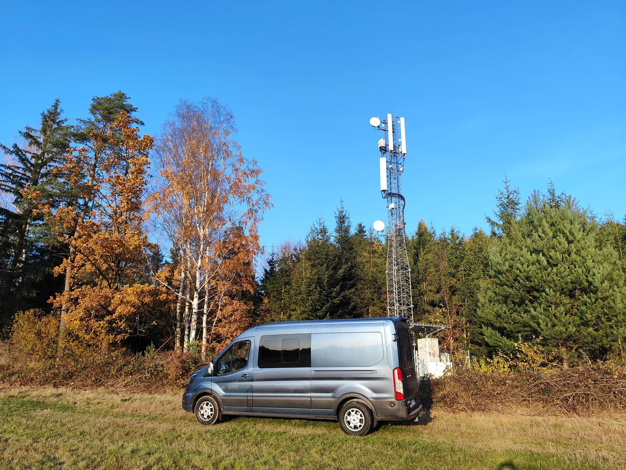 Telekomunikační stožár s anténní technologií na okraji lesa